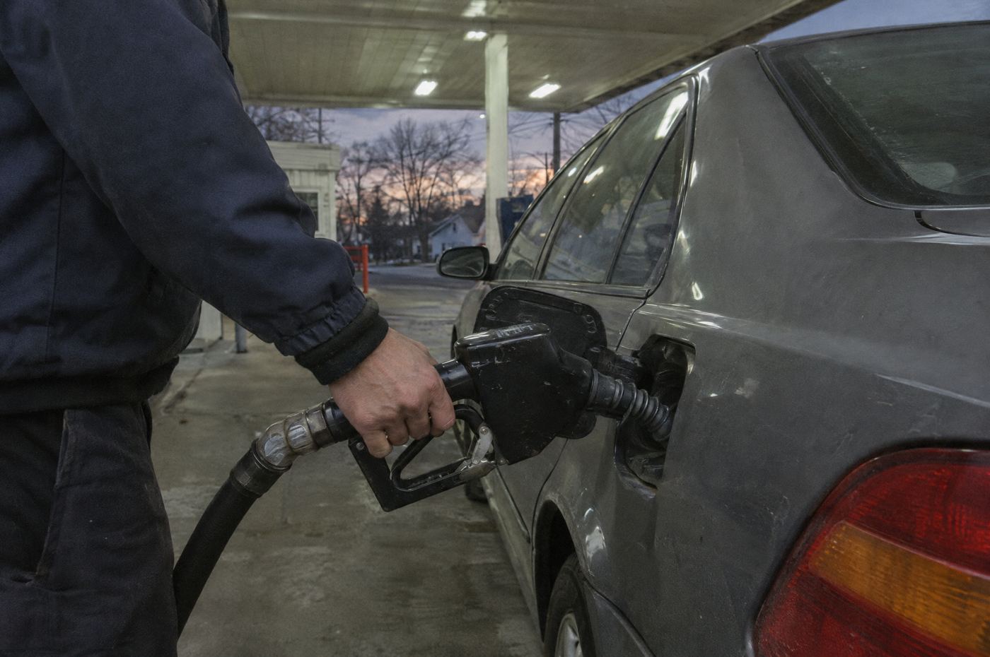 A driver filling up a sedan at a gas station at dusk